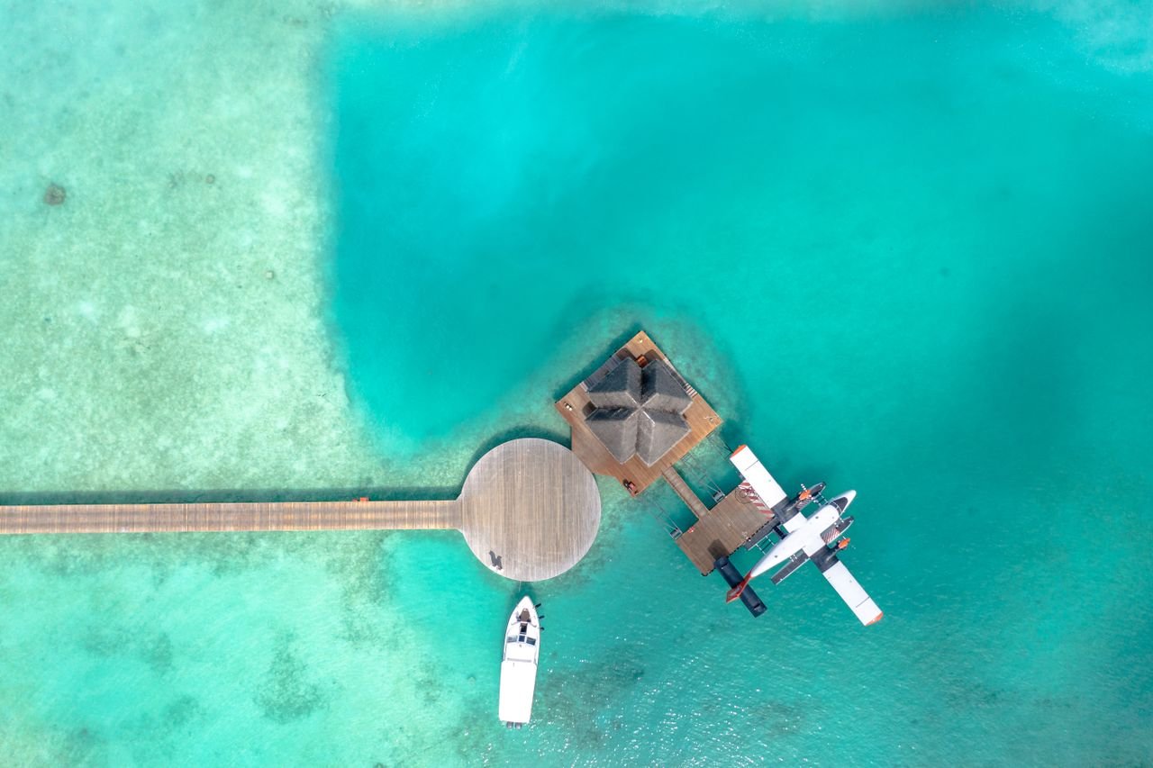 A stunning aerial photo of a seaplane docked at a pier in the Maldives with turquoise waters.
