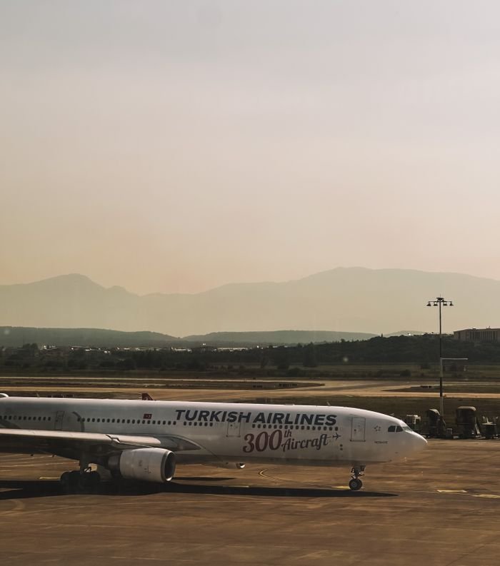Turkish Airlines airplane parked at the airport tarmac with mountains in the background. travel company international