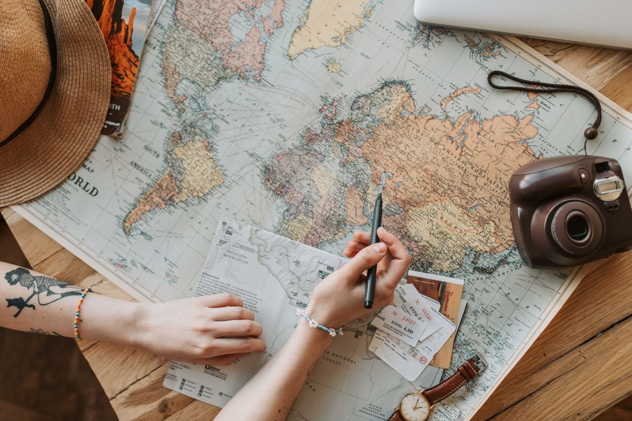 Top view of a woman's hands planning a trip with a map, camera, and travel items best international travel agency