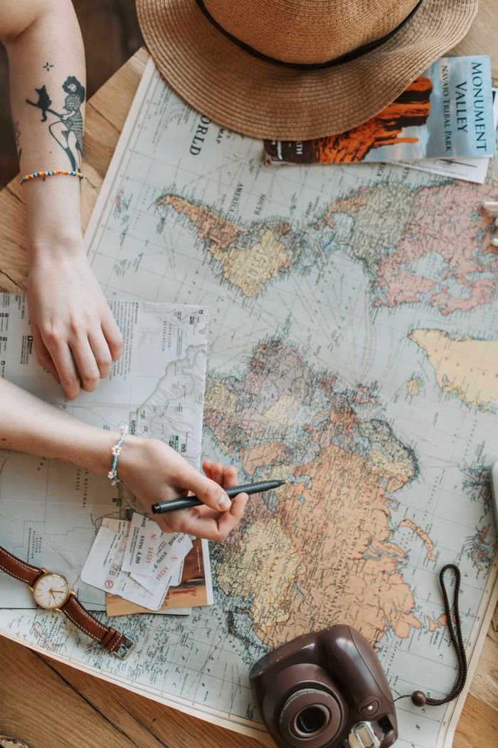 Person planning a journey with a world map, camera, and travel guide on a wooden table foreign travel agency