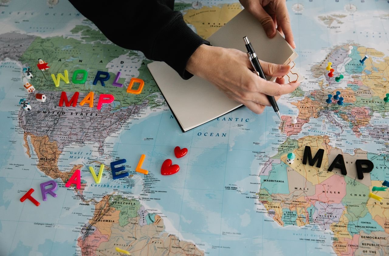 Hands holding pen and notebook over vibrant world map planning a journey best international travel agency